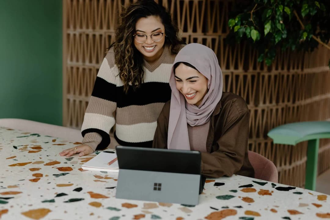 two women sitting at a table with a laptop
